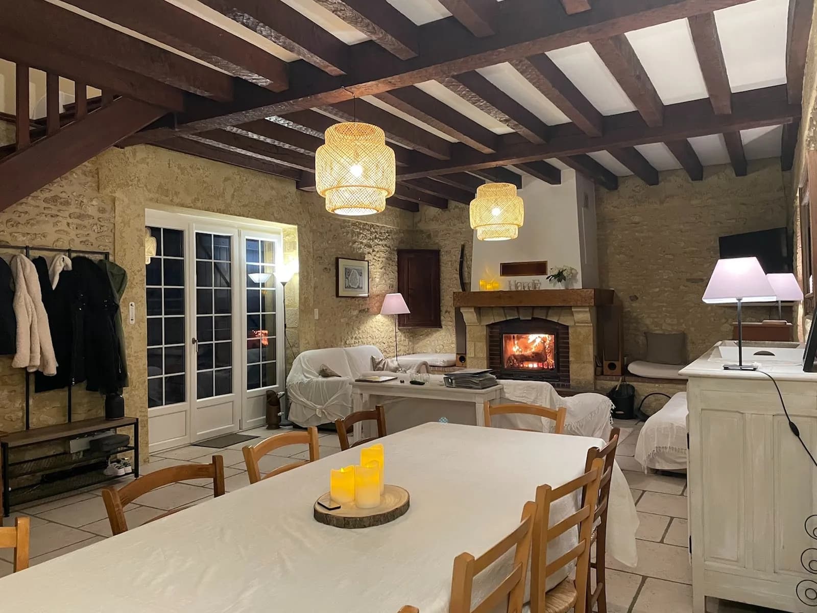 Salon-séjour en pierres apparentes avec cheminée allumée, en soirée